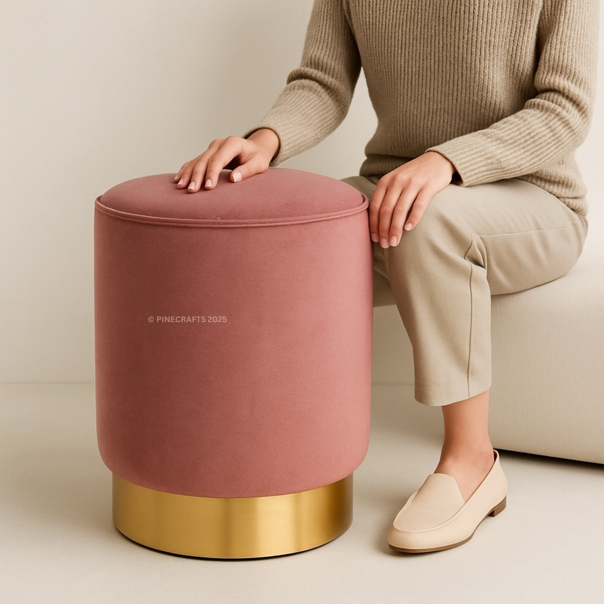 Person sitting on a pink ottoman with gold base against a neutral background